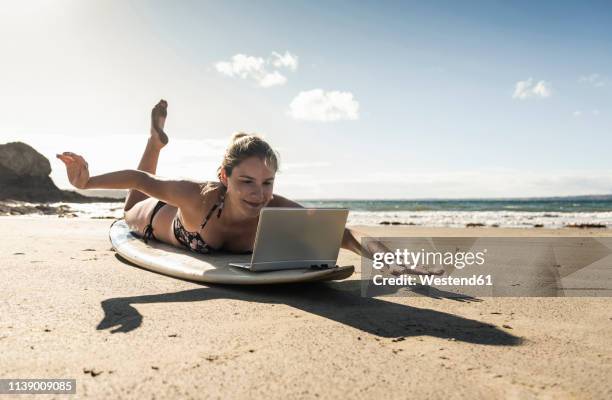 young woman lying  on surfboard, using laptop - surfing the net fotografías e imágenes de stock