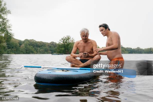 older and younger man with sup board on a lake using cell phone - crazy dad stock pictures, royalty-free photos & images