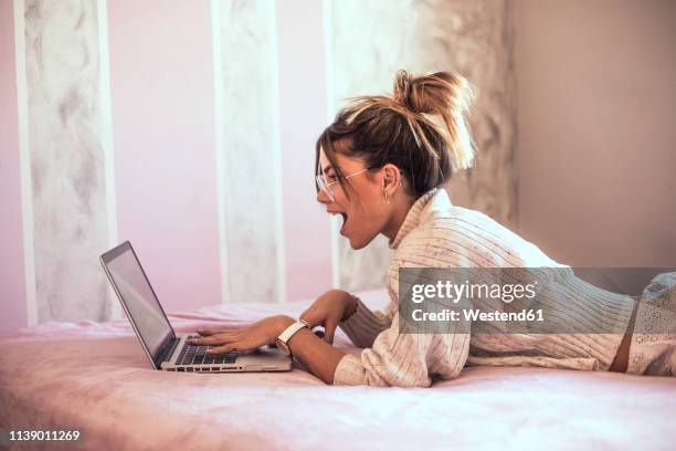 surprised young woman lying on bed using laptop - frau in slip stock-fotos und bilder