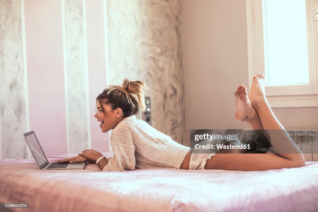 Surprised young woman lying on bed using laptop