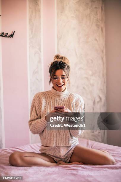 portrait of young woman sitting on bed text messaging - victoria's secret stock pictures, royalty-free photos & images