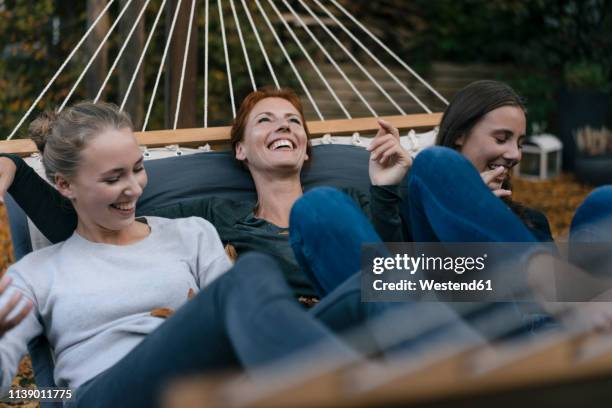 carefree mother with two teenage girls lying in hammock in garden in autumn - familie jugendlicher zufrieden stock-fotos und bilder