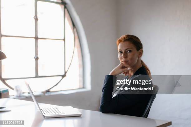 portrait of businesswoman with laptop sitting at desk in office - blazer jacket stockfoto's en -beelden