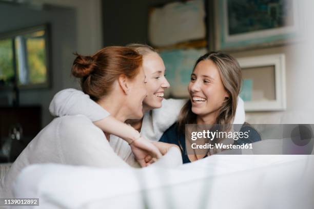 happy teenage girl hugging mother and sister on couch at home - mother adult daughter stock-fotos und bilder