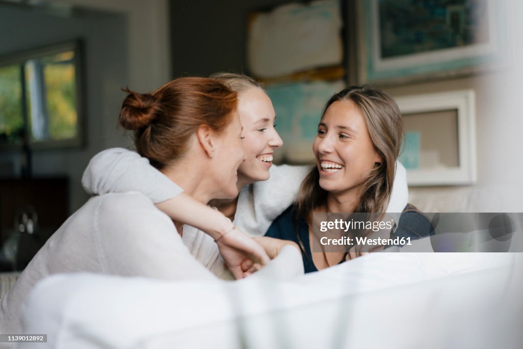 Happy teenage girl hugging mother and sister on couch at home