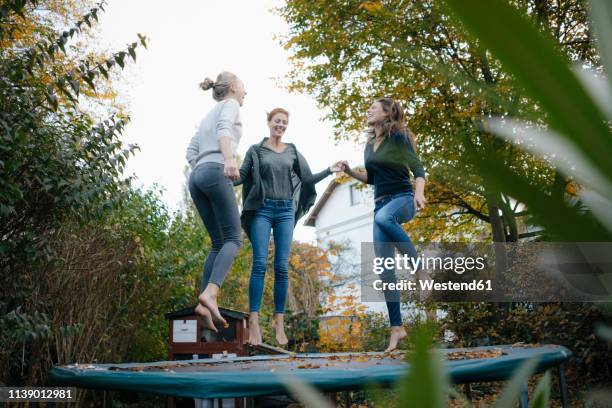 happy mother with two teenage girls jumping on trampoline in garden in autumn - trampoline photos et images de collection