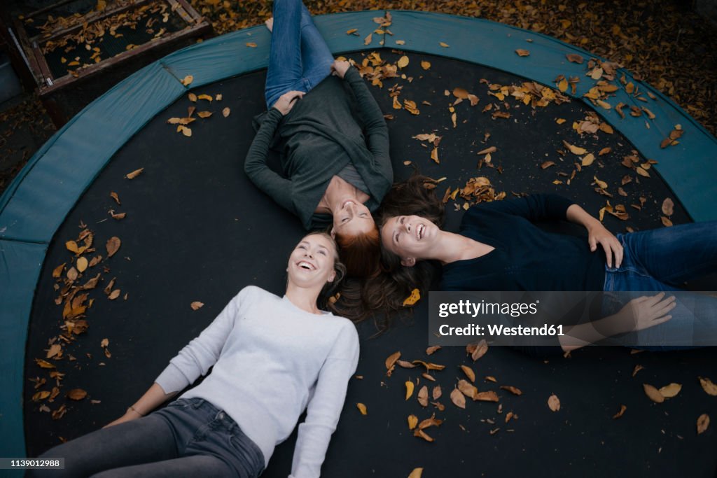 Happy mother with two teenage girls lying on trampoline in autumn