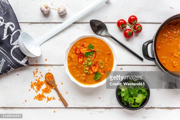bowl and pot of garnished red lentil soup and ingredients on white wood - lentil stock-fotos und bilder