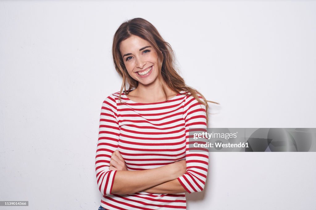 Portrait of laughing young woman wearing red-white striped shirt against white background