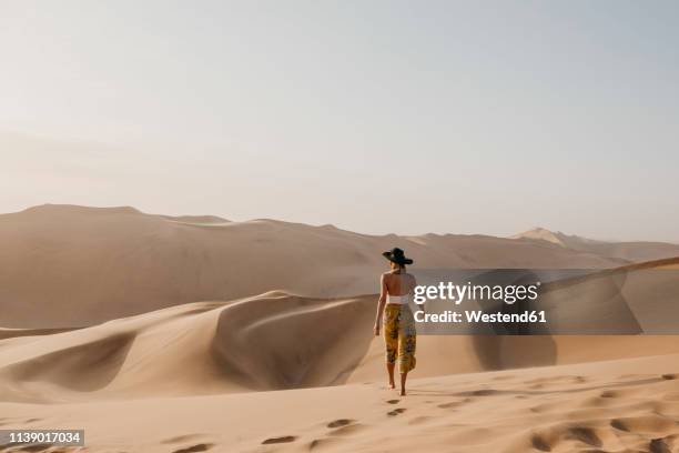 namibia, namib, back view of woman walking barefoot on desert dune - namibia women stock pictures, royalty-free photos & images