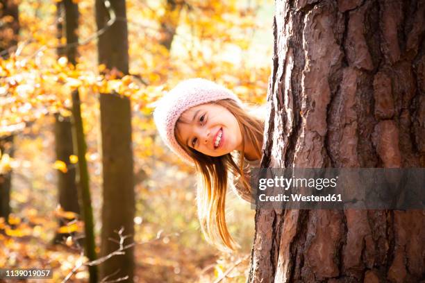 young girl behind tree in autumn - girl hiding behind bush stock pictures, royalty-free photos & images