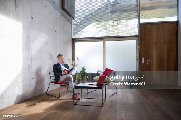 businessman sitting in a loft at concrete wall reading book - sitting chair office relax stockfoto's en -beelden