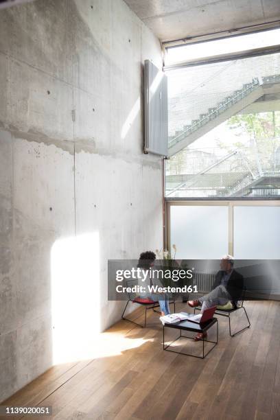 businessman and businesswoman sitting in a loft at concrete wall talking - meeting room stock-fotos und bilder