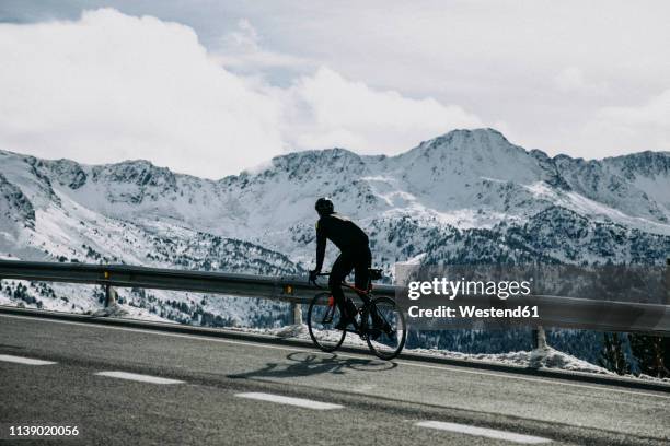 andorra, cyclist on mountain road with snowy mountains in the background - winter cycling stock pictures, royalty-free photos & images