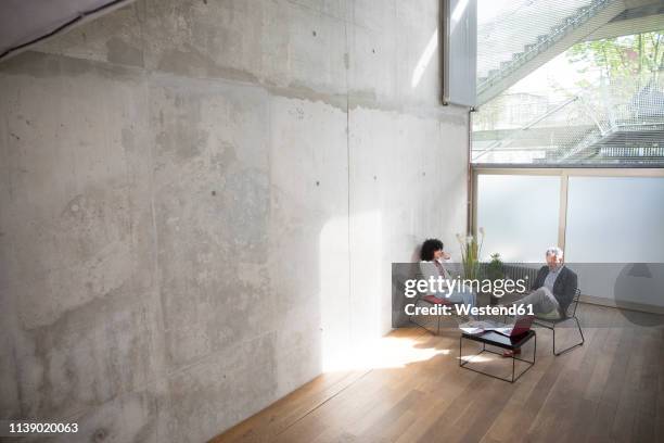 businessman and businesswoman sitting in a loft at concrete wall - apartamento tipo loft fotografías e imágenes de stock