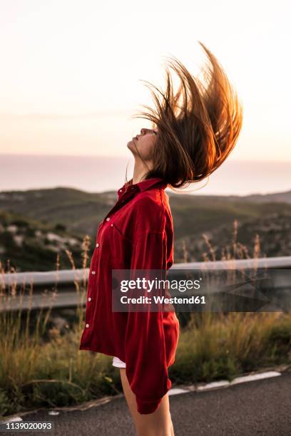 young woman tossing her hair on country road at sunset - sacudir el pelo fotografías e imágenes de stock