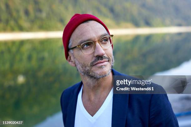 portrait of bearded mature man wearing glasses and red cap in nature - menswear stock-fotos und bilder