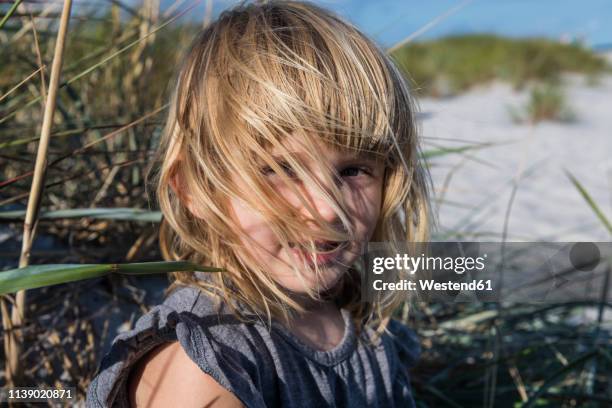 denmark, bornholm, portrait of smiling girl on dueodde white sand beach - girl blowing sand stock-fotos und bilder