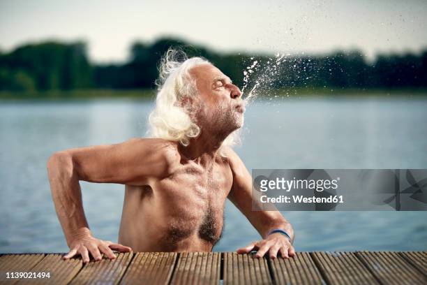 senior man with white hair leaning on jetty splashing with water - boardwalk stock-fotos und bilder