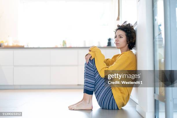 serious woman sitting on floor leaning against a wall at home - pessimism stock pictures, royalty-free photos & images