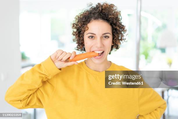 portrait of woman eating a carrot at home - möhre stock-fotos und bilder