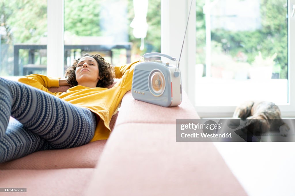 Woman lying on couch listening to music with portable radio at home