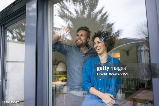 happy couple behind window at home looking out - man woman top view stockfoto's en -beelden