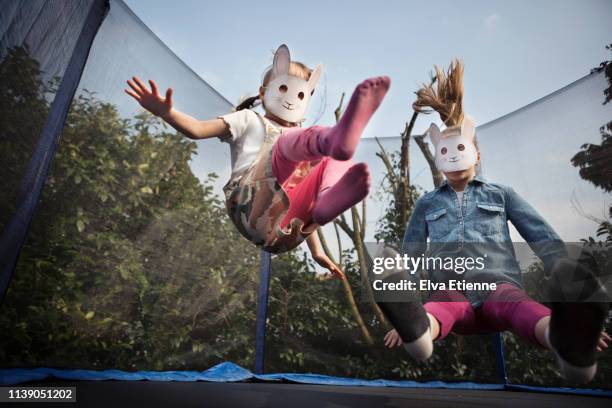 two children wearing rabbit masks and bouncing on a trampoline - family no faces stockfoto's en -beelden