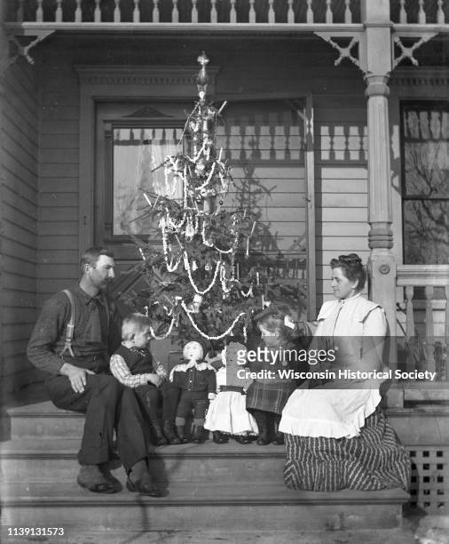 The Alexander Krueger family sitting on a porch in front of a decorated Christmas tree, Emmet, Wisconsin, 1902. Alexander and Edgar are sitting on...