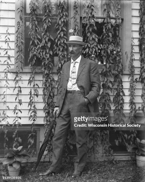 Outdoor portrait of Alexander Krueger standing in front of the ivy-covered windows of a house, Emmet, Wisconsin, 1904. He is wearing a hat and has...