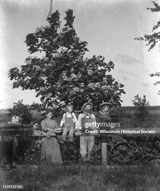 Outdoor portrait of the Alexander Krueger family posing along a fence in front of a Catalpa tree, Emmet, Wisconsin, 1908. Jennie and Edgar Krueger...