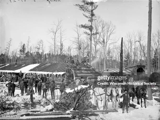 Elevated group portrait of loggers at a logging camp posing in the snow, Black River Falls, Wisconsin, 1890. Some of the men are posing on the roof...