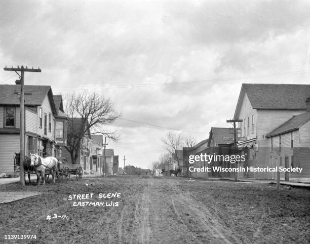 View down an unpaved street, Eastman, Wisconsin, 1911. A horse and carriage is tied to a post on the left. A saloon and hotel, and the Park Hotel are...