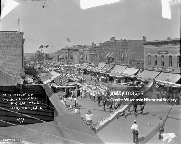 Rooftop view of a parade passing through downtown Viroqua, Viroqua, Wisconsin, August 24, 1922. A boy is sitting on a roof on the left, looking down...