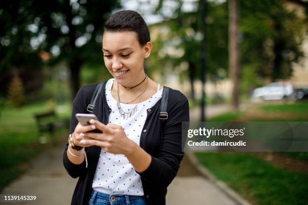 vrouwelijke student sms op haar mobiele telefoon buitenshuis - college application stockfoto's en -beelden