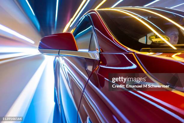 electric powered car drives on city street while night - car industry stock-fotos und bilder