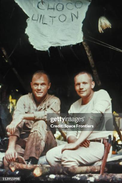 American astronauts John Glenn and Neil Armstrong during survival training in the Darien rainforest of Panama, circa 1963. Above them is a sign...