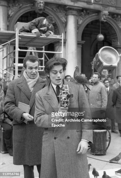 French actor Alain Delon playing with a cinecamera during the unfinished Marco Polo movie shooting in S.Mark Square in Venice, a pigeon on his...