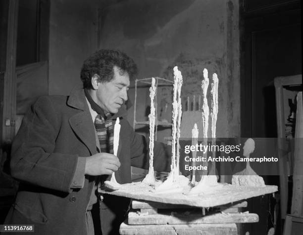 Swiss sculptor Alberto Giacometti in his parisian studio finishing a sculpture,wearing a woolen coat and a striped scarf, Paris 1950.