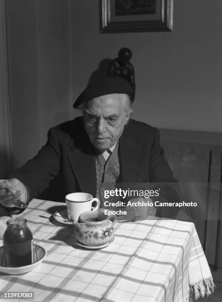 Italian futurist painter Carlo Carrà having breakfast with a cup of coffee, some bread and jam, wearing a beret, a woolen cardigan and a blazer,...
