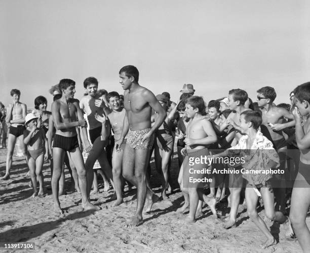 Italian actor and singer Adriano Celentano, wearing a swimming suit andwalking on the Lido beach, chased by a crowd of children and teenagers, Venice...