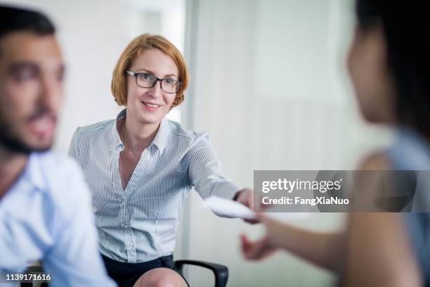 businesswoman passing document to colleague - passing imagens e fotografias de stock