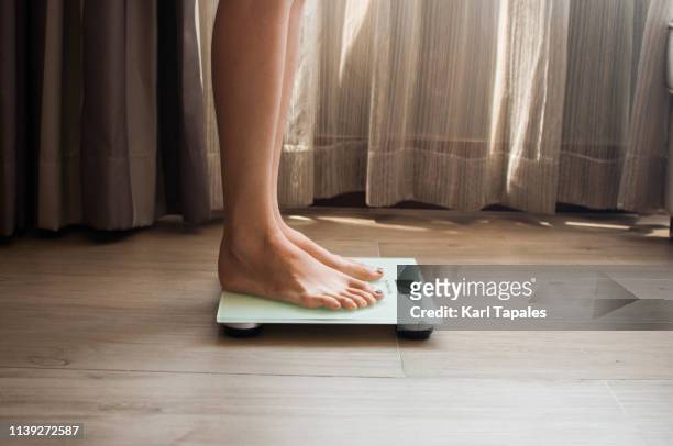 a young woman is weighing herself in a weighing scale - balança imagens e fotografias de stock