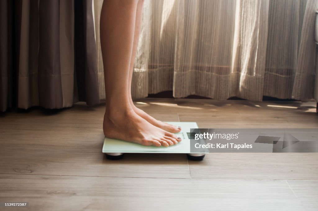 A young woman is weighing herself in a weighing scale