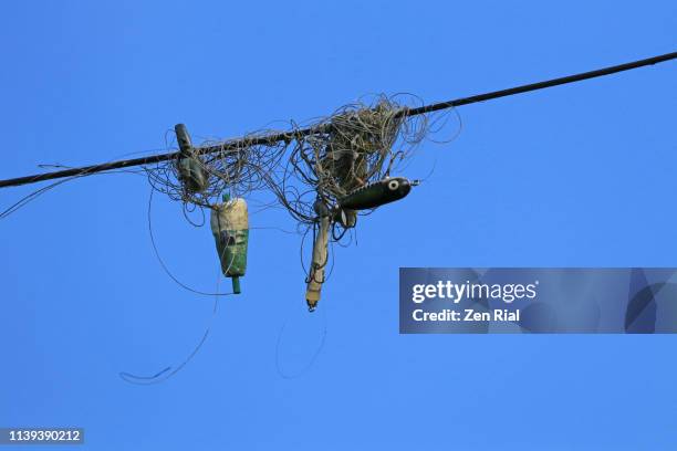 fishing lines and lures tangled up in a powerline against blue sky - lenza foto e immagini stock