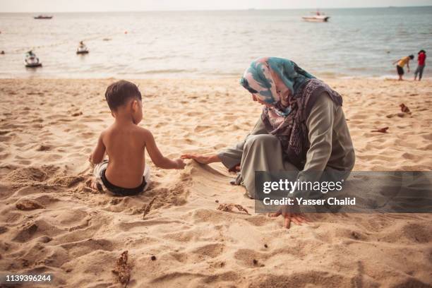 little boy and mother play on a beach - muslim woman beach stock-fotos und bilder