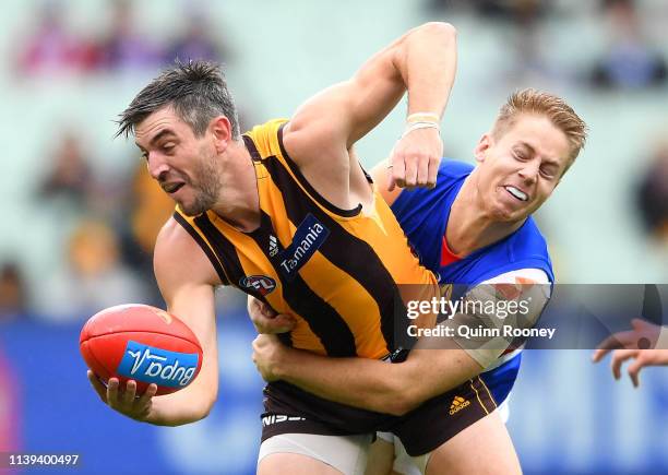 Ricky Henderson of the Hawks handballs whilst being tackled by Lachie Hunter of the Bulldogs during the round two AFL match between the Hawthorn...