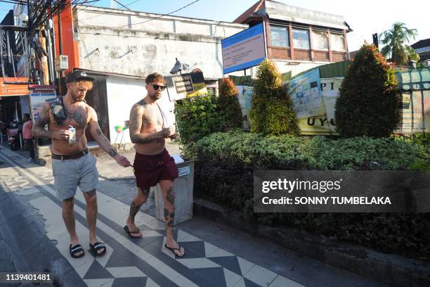 Tourists walk past a building permit board at the site of the Sari Club, which was hit in the 2002 bombings, in Kuta near Denpasar on the resort...