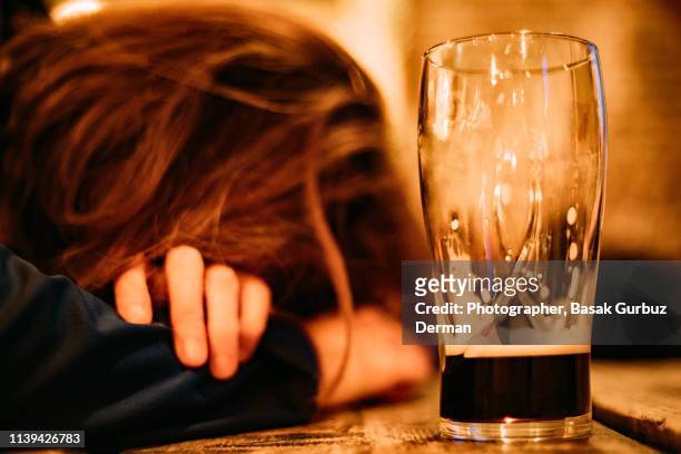 young drunk woman sleeping on bar counter drinking dark beer - alcolismo foto e immagini stock