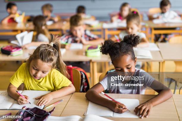 des écolières heureuses écrivant une dictée sur une classe à l’école. - bureau écolier photos et images de collection